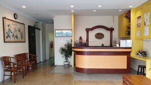 A reception area with a wooden reception desk, chairs, a potted plant, and a wall-mounted clock. - Fully Hotel Johor Jaya (Johor Bahru)