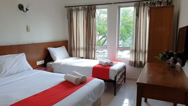 A hotel room with two beds, a wooden headboard, a small table, and a view of the outdoors through large windows. - Fully Hotel Johor Jaya (Johor Bahru)