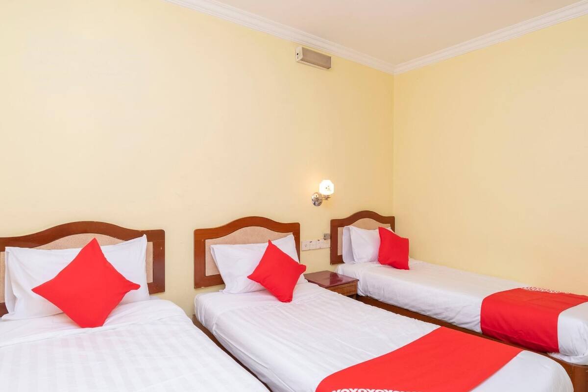 Une chambre d’hôtel avec trois lits simples, chacun doté de draps blancs et d’oreillers rouges.