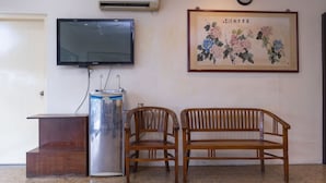 A room with a wooden bench, a television mounted on the wall, an air conditioning unit, and a framed artwork above a clock. - Fully Hotel Johor Jaya (Johor Bahru)