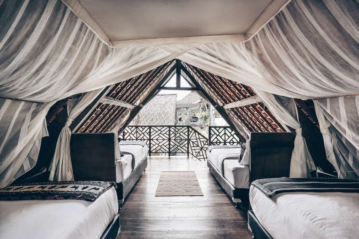 A cozy, triangular-roofed room with two beds and a view of a garden.