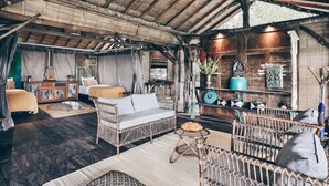 Une pièce rustique avec un plafond haut, des meubles en osier et une étagère en bois ornée d’objets décoratifs.