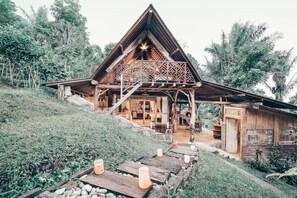 Une cabane en bois avec un toit triangulaire, une véranda dotée de balustrades en bois et un chemin de pierre menant à l’entrée.