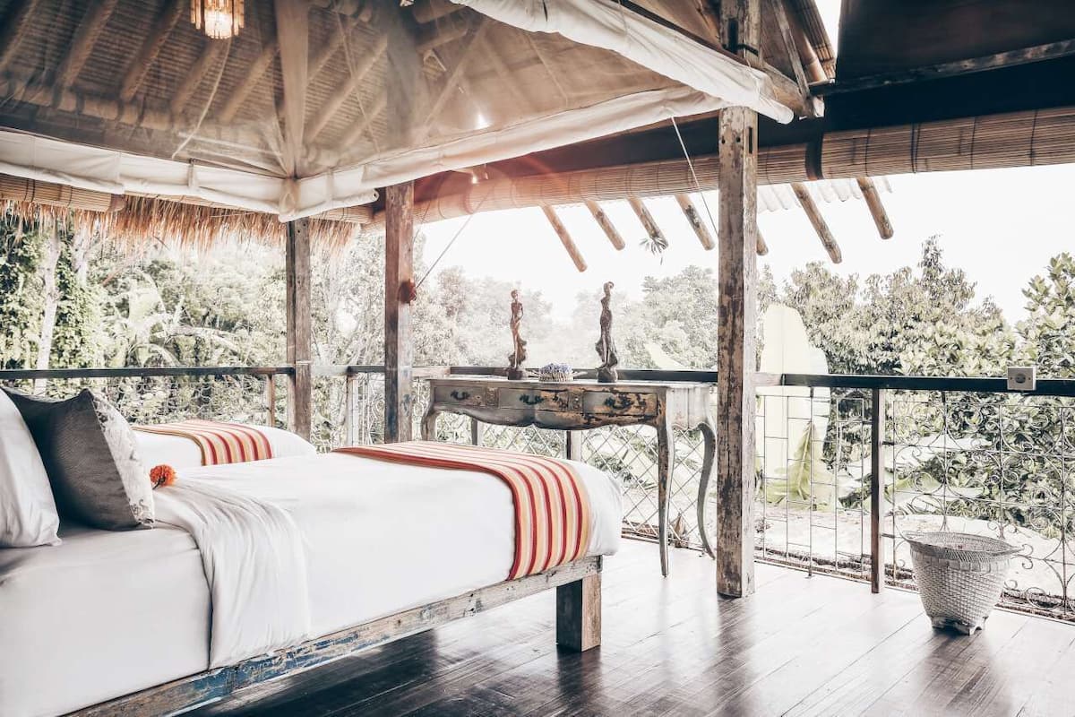A bedroom with a bed, a wooden table, and a view of the outdoors.