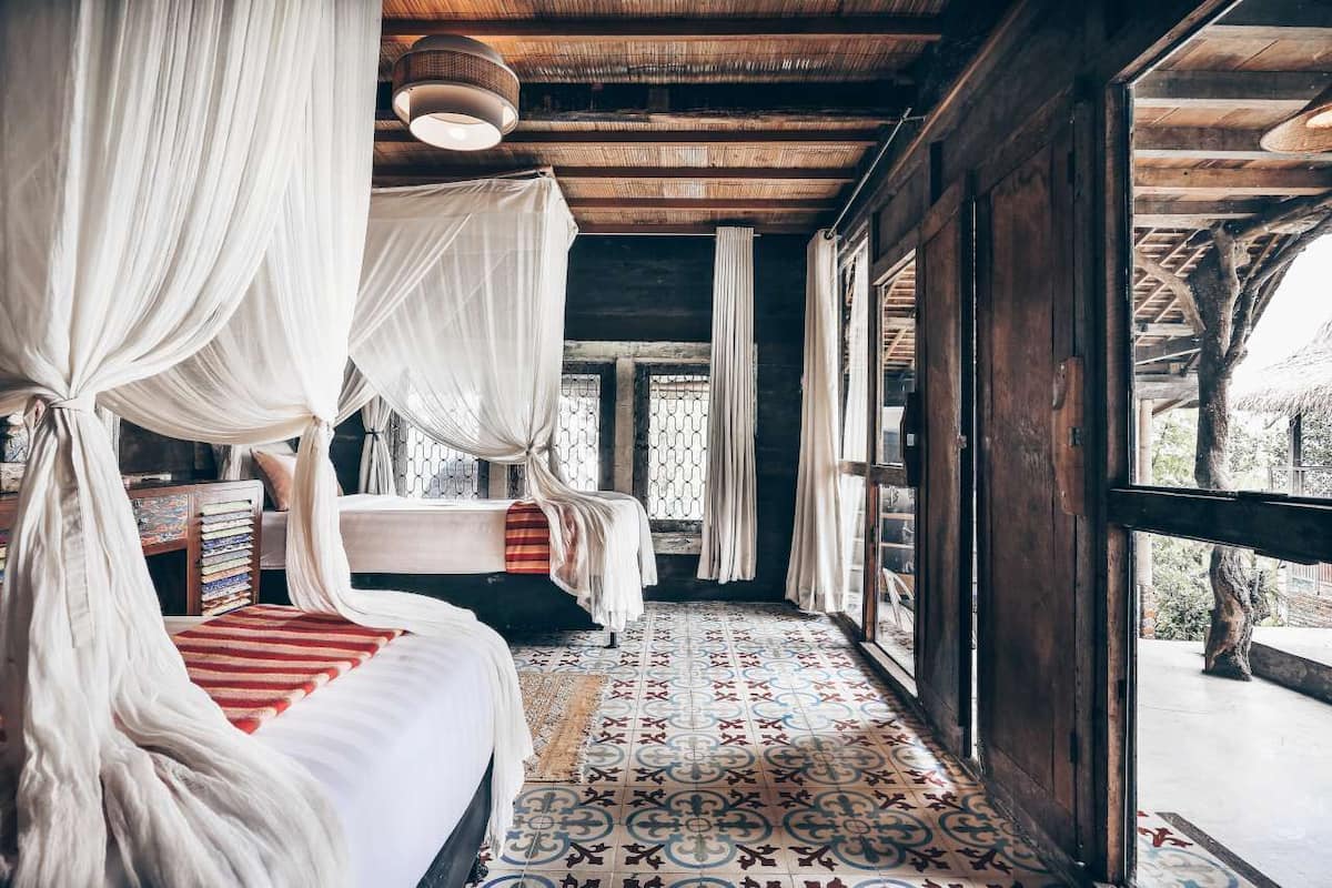 A room with a bed under a canopy, a patterned floor, and a view through large windows.