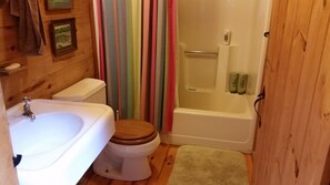 Un baño con piso de madera, un lavamanos blanco, un inodoro y una zona de ducha.