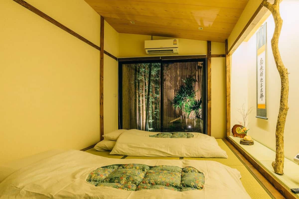 A traditional Japanese-style room with tatami flooring, a sliding door leading to a balcony, and a small table with a vase and a clock.
