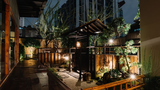 A well-lit outdoor garden area with a wooden pathway, stone steps, and a bamboo fence. - MAYU Bangkok Japanese Style Hotel (Bangkok)