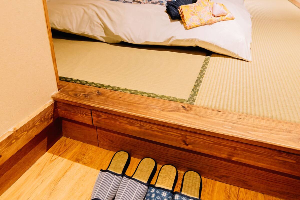 A traditional Japanese-style room with tatami flooring, a bed with a futon, and a pair of slippers.