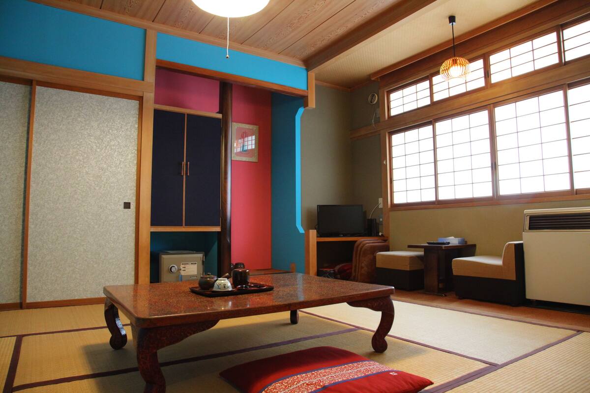A traditional Japanese room with tatami flooring, a low table with tea set, sliding doors, and a television.