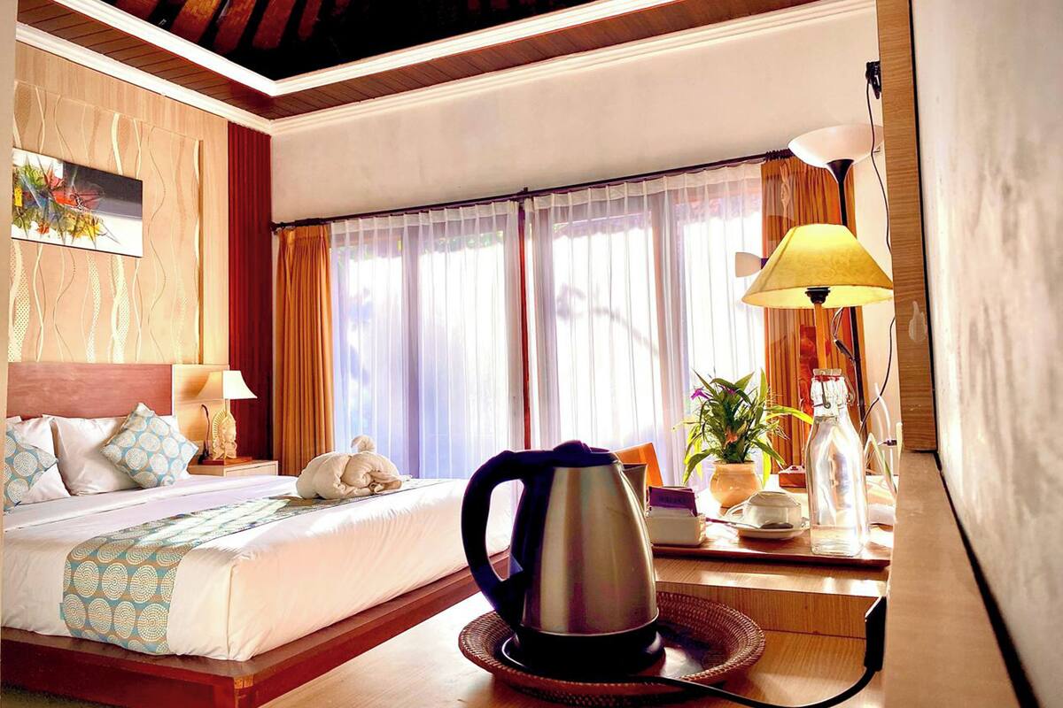 Une chambre d’hôtel avec un lit, une machine à café, une lampe et une fenêtre avec des rideaux.