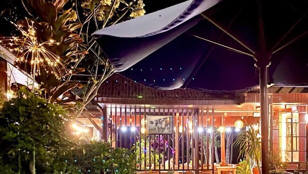 Un área de piscina al aire libre con una terraza de madera, plantas en macetas y una zona de estar cubierta.