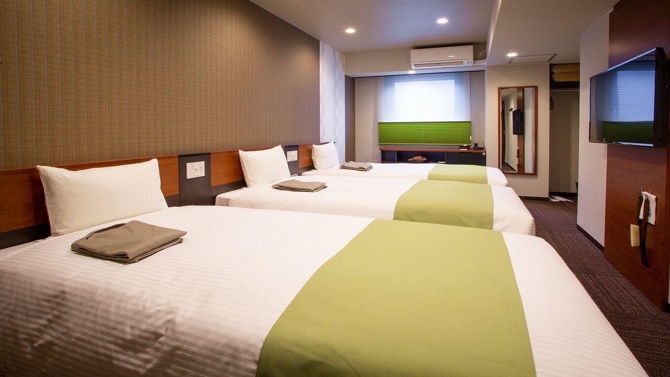 A hotel room with two beds, a television, a mirror, and a window with blinds.