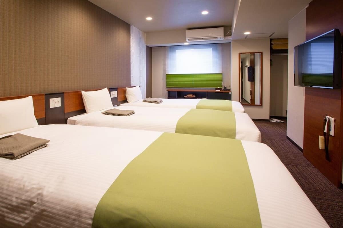 A hotel room with two beds, a television, a mirror, and a window with blinds.