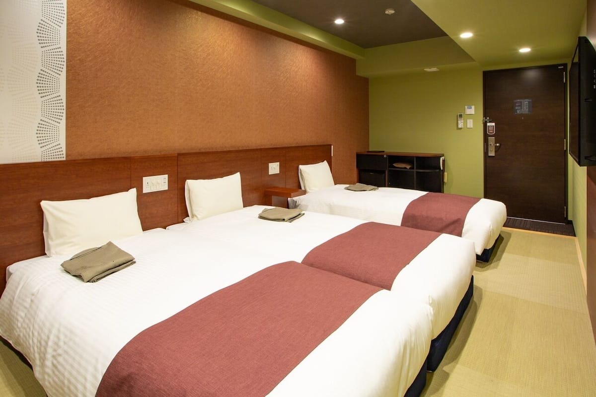A hotel room with two beds, a television, a desk, and a door.