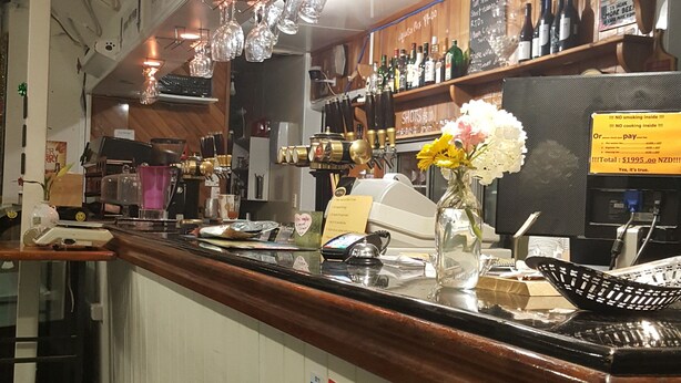 A reception area with a counter, a sign reading "RECEPTION", and various items like a vase with flowers, a cash register, and a menu board.