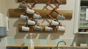 A kitchen with a wooden rack holding mugs, a blue dish rack, a bottle of hand soap, and a box of tea bags.