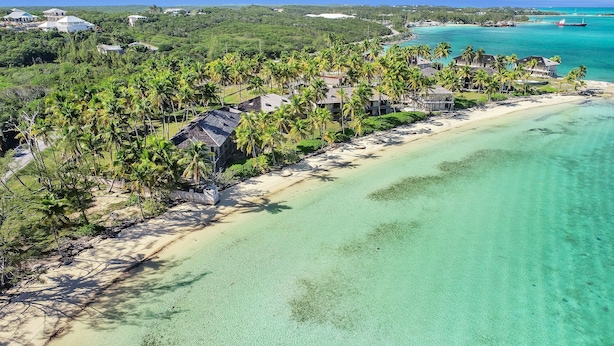 An aerial view of a beach resort with multiple bungalow-style accommodations, clear turquoise waters, and lush greenery. - Ixora West - Views over Elizabeth harbor, beach access across the road. (George Town)