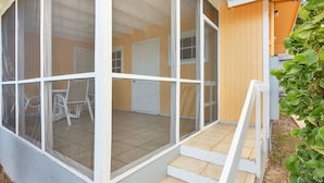 A covered outdoor area with a staircase leading to a door, surrounded by a fence and vegetation. - Ixora West - Views over Elizabeth harbor, beach access across the road. (George Town)