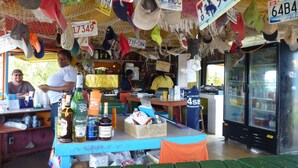 A small roadside stand with a variety of hats and license plates hanging above the counter. - Ixora West - Views over Elizabeth harbor, beach access across the road. (George Town)