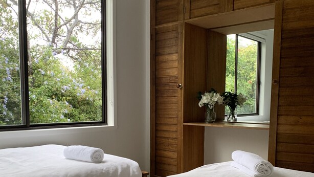 Un dormitorio con dos camas, un armario de madera y una ventana con vistas a árboles.