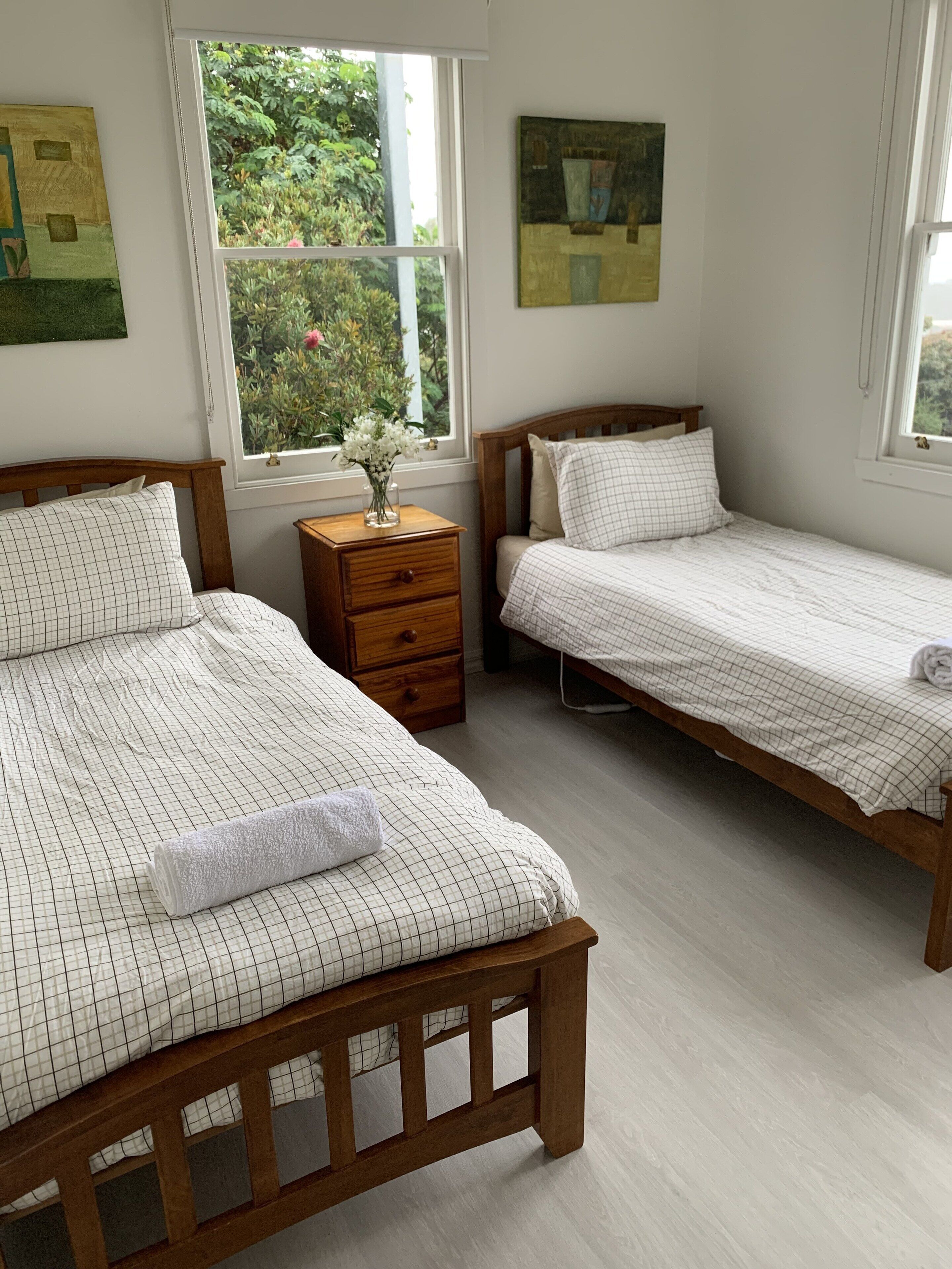 Un dormitorio con dos camas de madera, una mesita de noche y una ventana con vistas a zonas verdes.