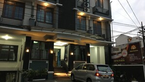 A multi-story hotel with a car parked in front, a staircase leading to the entrance, and a signboard advertising the hotel. - Hotel Kristina (Yogyakarta)