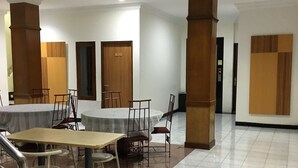 A spacious room with a large table and chairs, wooden pillars, and a tiled floor. - Hotel Kristina (Yogyakarta)