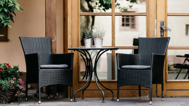 Two wicker chairs and a table outside a building with a wooden door and window. - Gasthof Hotel Kopf (Riegel am Kaiserstuhl)
