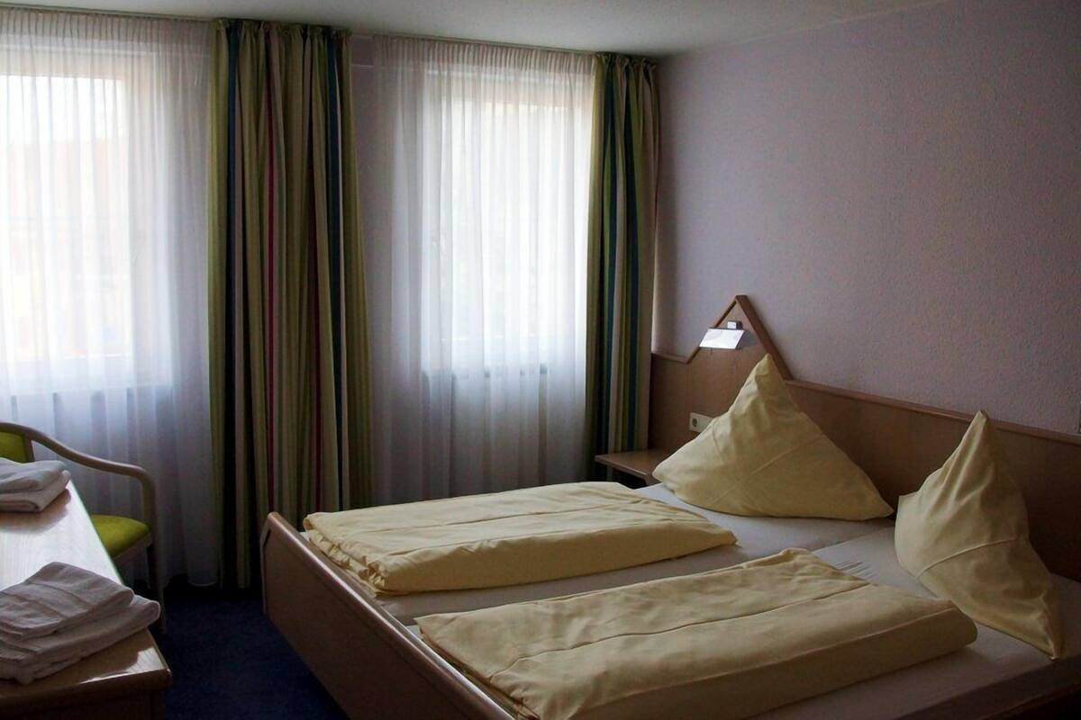 Une chambre d’hôtel avec un lit, une table de chevet, une chaise et une fenêtre avec des rideaux.