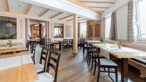 A spacious dining area with wooden tables and chairs, large windows with curtains, and a high ceiling with exposed beams. - Gasthof Hotel Kopf (Riegel am Kaiserstuhl)