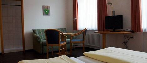 Ein Hotelzimmer mit zwei Betten, einem Schreibtisch mit Computer, einem Stuhl, einer Heizung und einem Fenster mit Vorhängen.