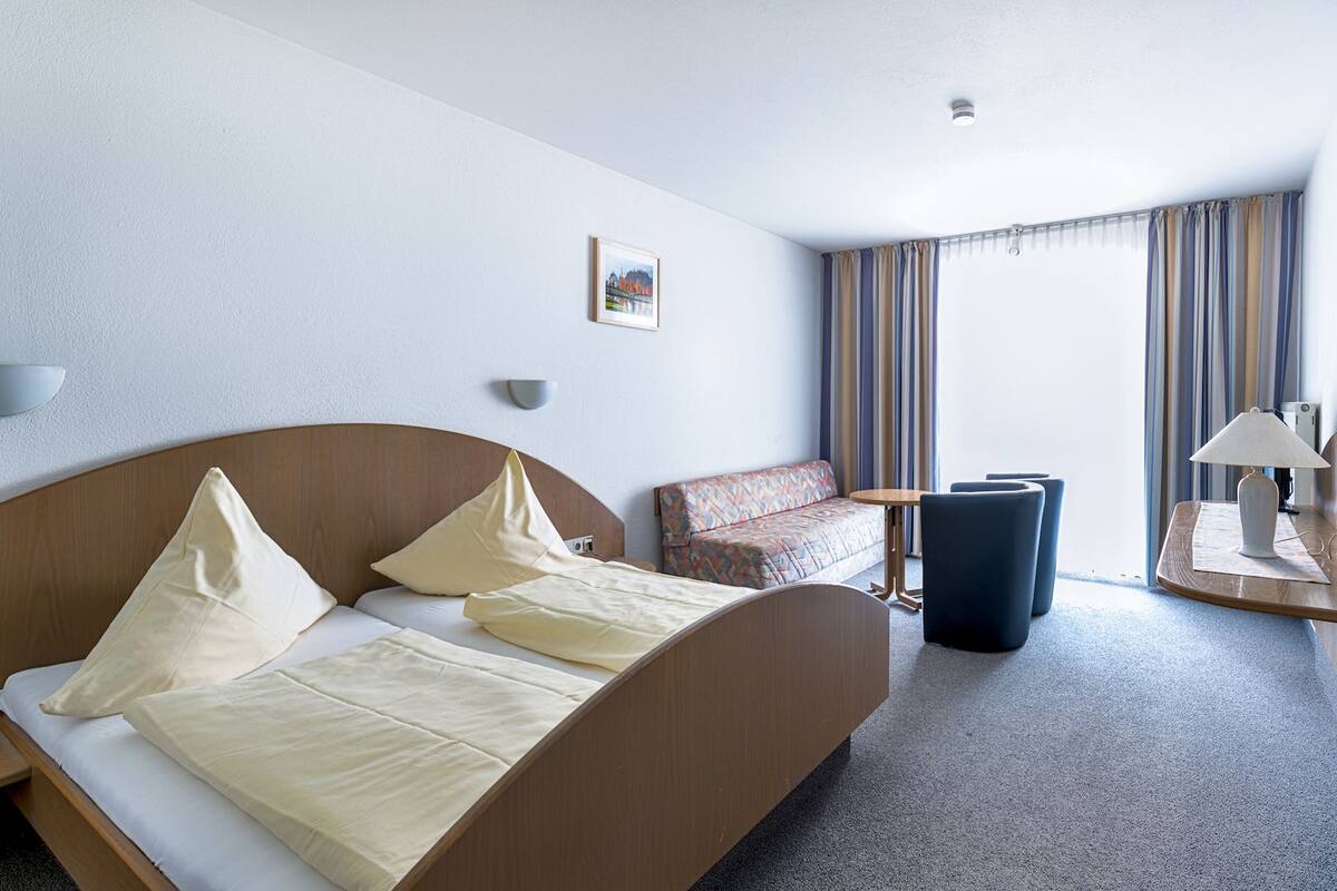 Une chambre d’hôtel avec un lit, un canapé, une petite table et une lampe.