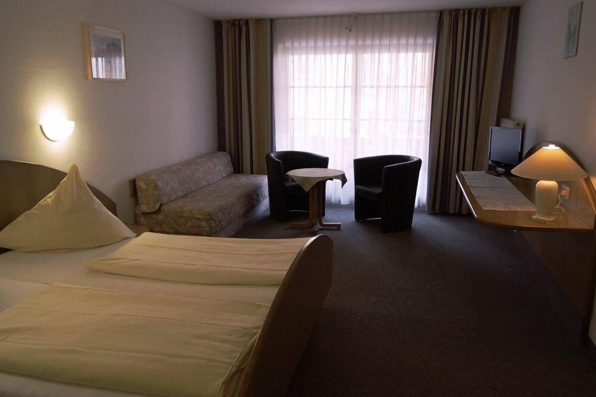 Une chambre d’hôtel avec deux lits, un canapé, une petite table ronde, deux fauteuils, un bureau avec une lampe et un téléviseur.