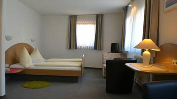 Een hotelkamer met een bed, een bureau met lamp, een stoel, een klein tafeltje, een televisie en een raam met gordijnen.