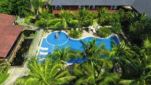 Un complexe hôtelier doté d’une piscine entourée de palmiers et d’un bâtiment surmonté d’un toit en tuiles.