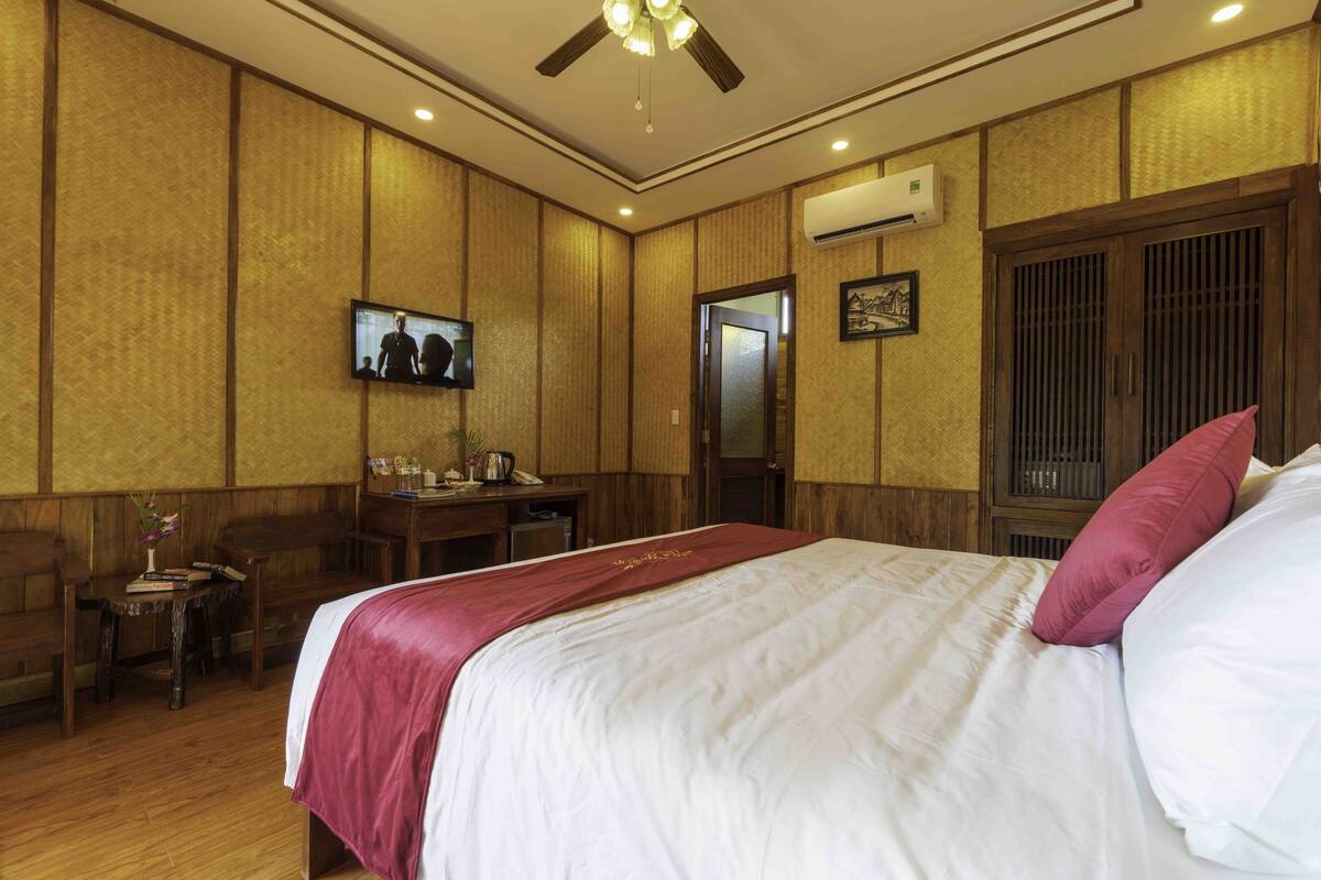 A hotel room with a bed, a desk, a television, and an air conditioning unit.