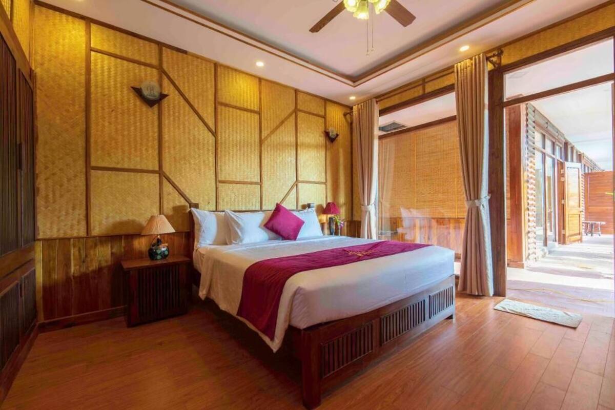 A hotel room with a bed, bedside tables, a ceiling fan, and a view through a glass door.