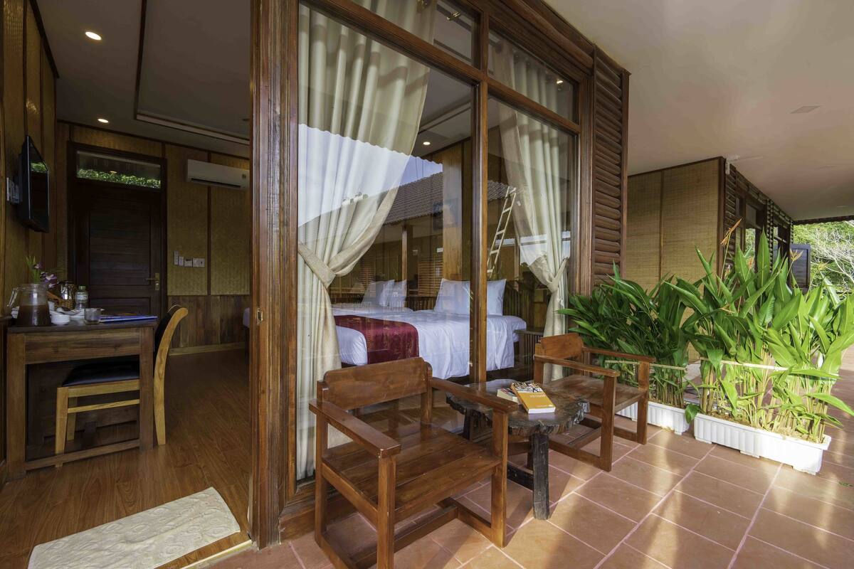 A room with a bed, wooden furniture, a desk, and potted plants.