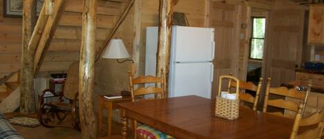 A wooden interior with a dining table, chairs, a bench, a lamp, a refrigerator, and a staircase.