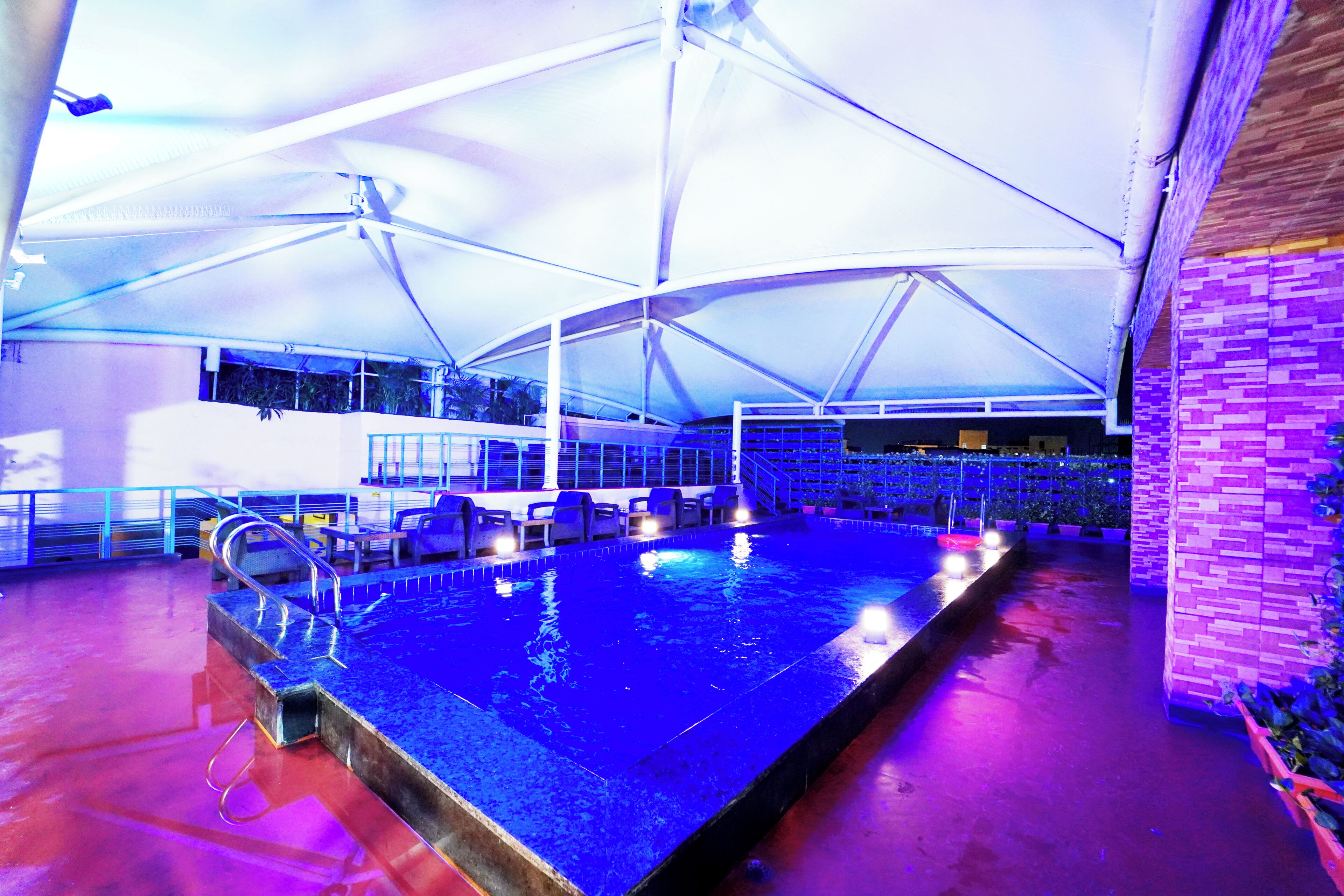 Una zona de piscina con toldo, asientos y un muro de ladrillo.