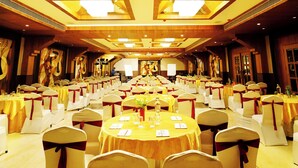 Uma sala de banquetes com mesas redondas, cadeiras com fitas vermelhas e teto alto com iluminação embutida.