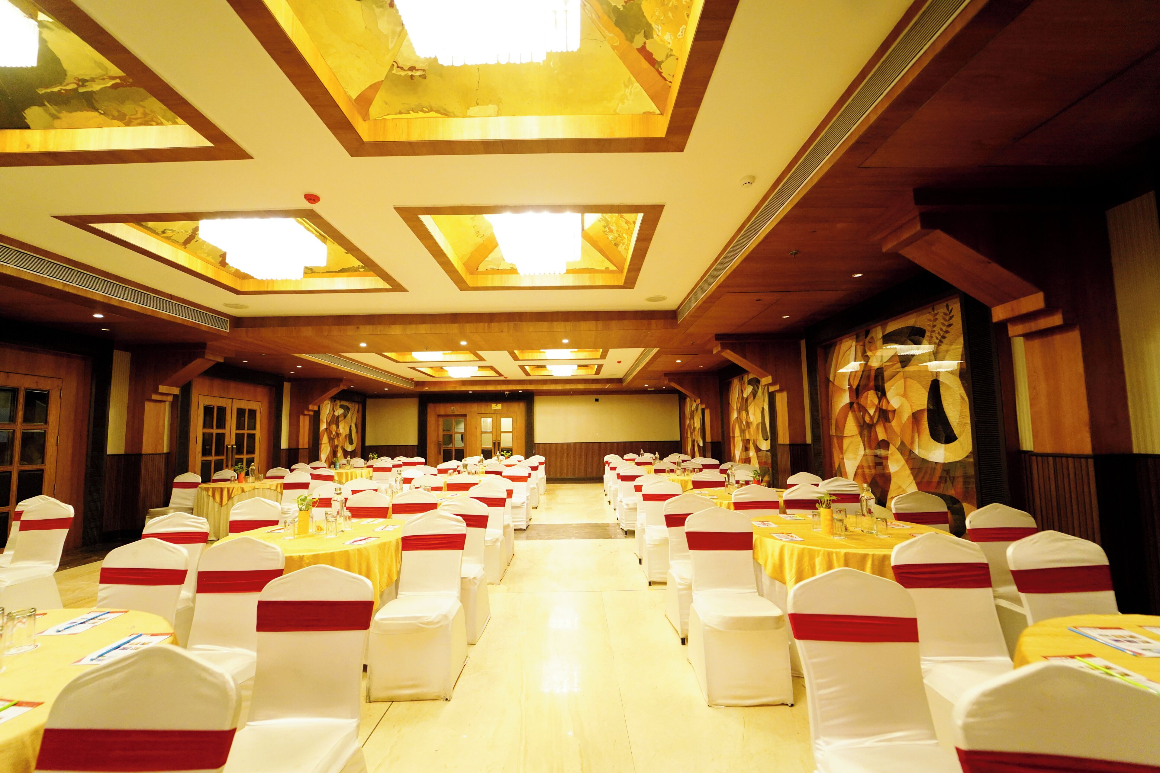Un salón de banquetes con filas de mesas y sillas, un techo alto con tragaluces y una pantalla grande al frente.