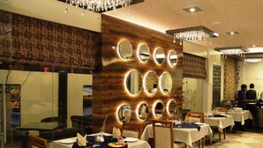 Restaurante com várias mesas, parede decorativa com espelhos e chão xadrez.