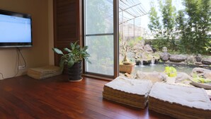 A room with a wooden floor, a television, a potted plant, and a view of a garden with rocks and a pond. - Memory Garden Villa (Luodong)