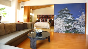 A modern hotel room with a wooden ceiling, a large bed, a sofa, a round table with a flower vase, and a cherry blossom painting on the wall. - Memory Garden Villa (Luodong)