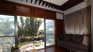 A living room with a large sliding glass door leading to a garden with a pond and waterfall. There is a sofa and a wooden table with a teapot and cups. - Memory Garden Villa (Luodong)