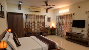 A hotel room with a bed, two chairs, a desk, a television, and a ceiling fan. - Tigers Heaven Resort (Chimur)