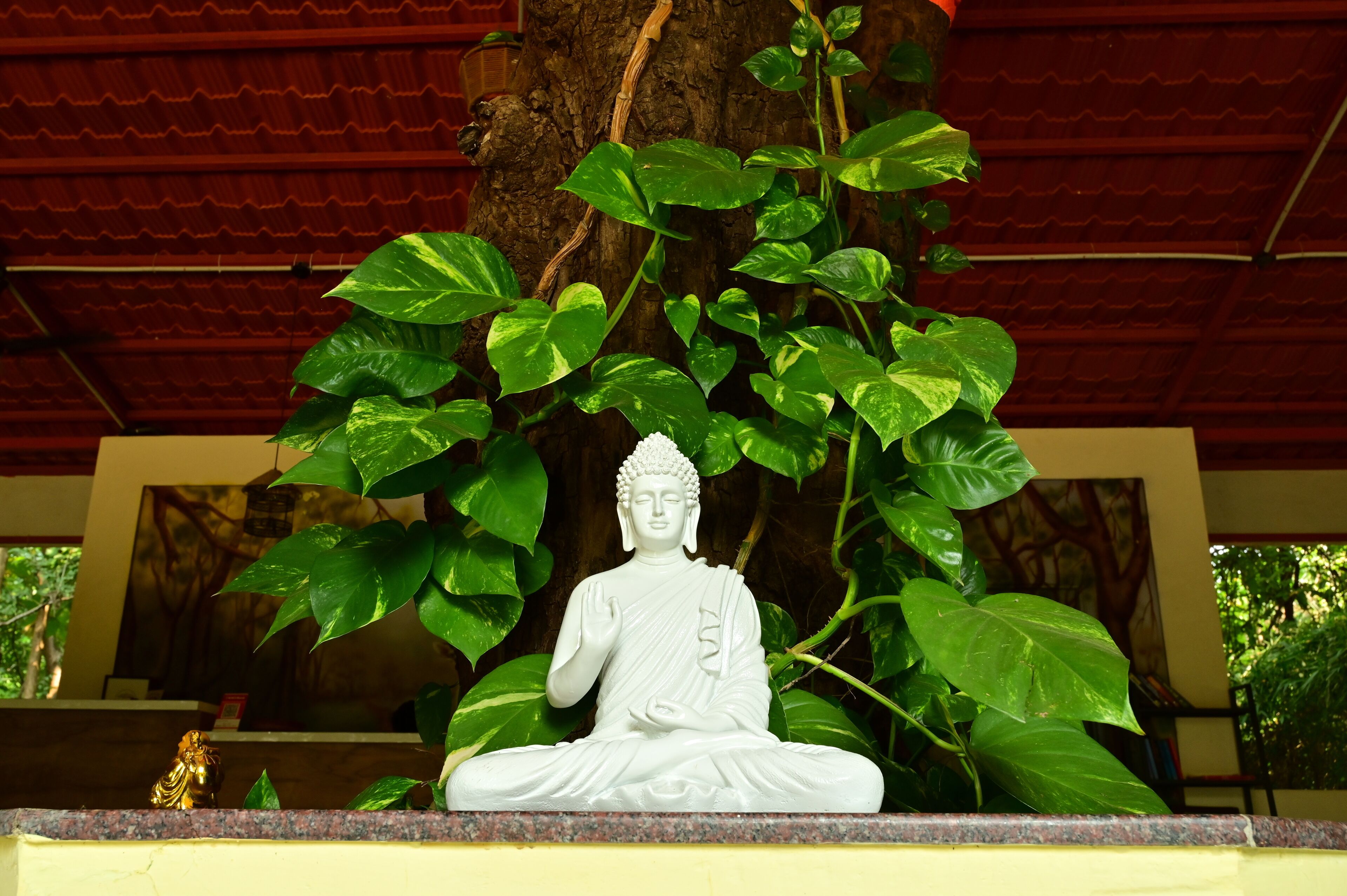 A statue of a seated figure in a meditative pose, surrounded by lush green foliage.