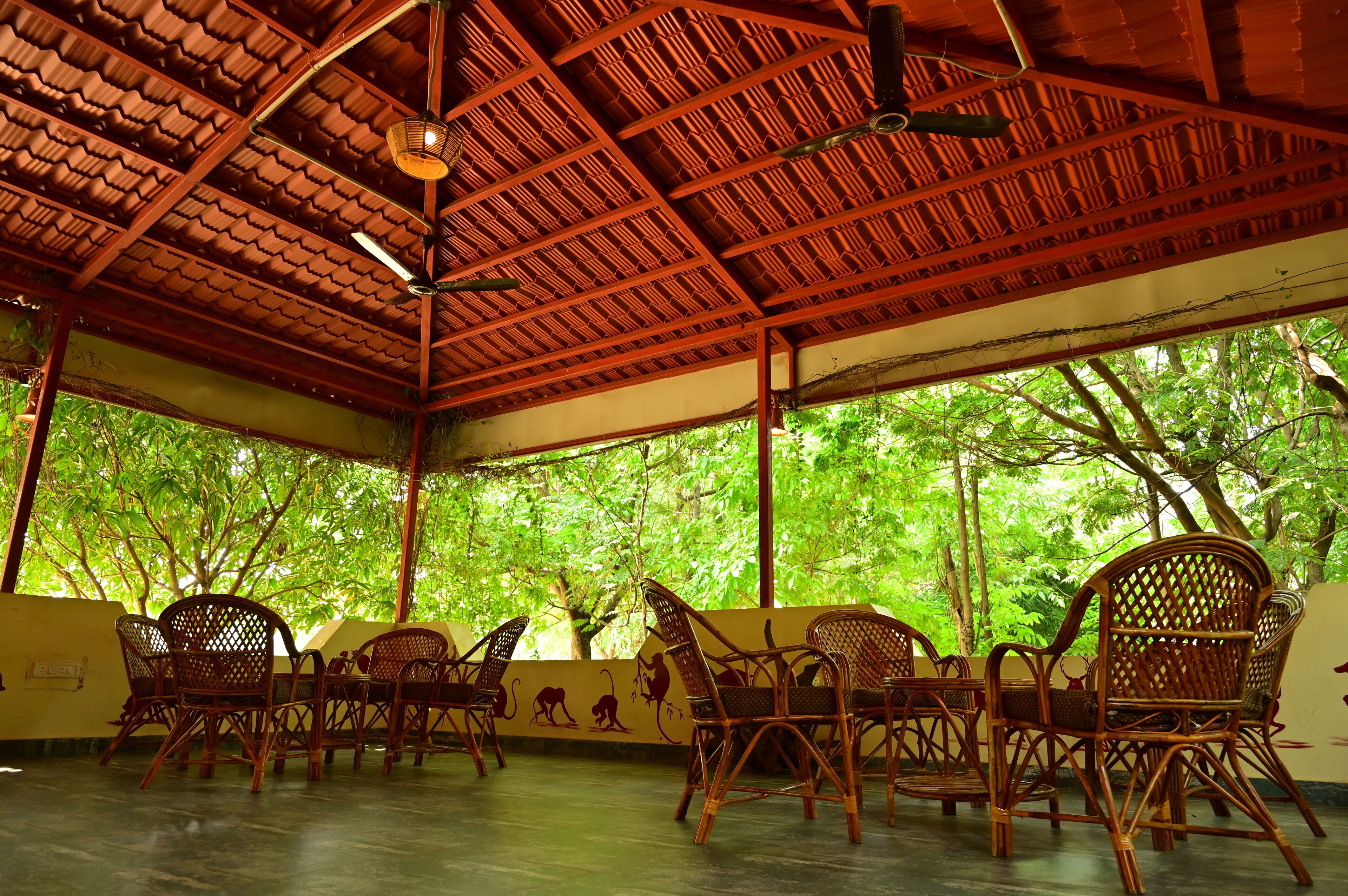 An outdoor covered seating area with wooden furniture and a view of lush green trees.